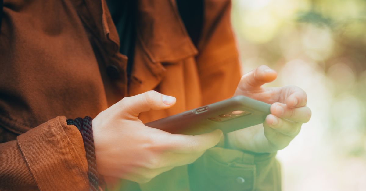 Close-up of hands using a smartphone outdoors with an autumn vibe, showcasing technology and nature.
